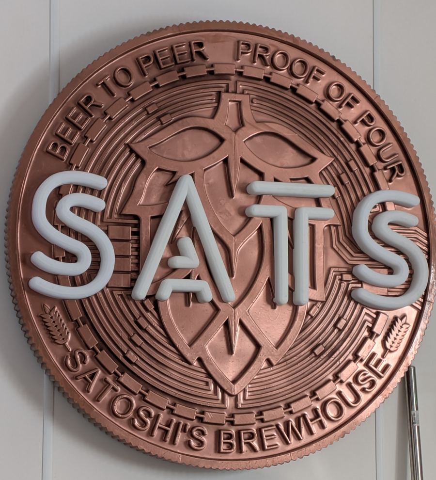 The satsbrew wall sign: a copper coin reading SATS, Beer to Peer, Proof of Pour, Satoshi's Brewhouse